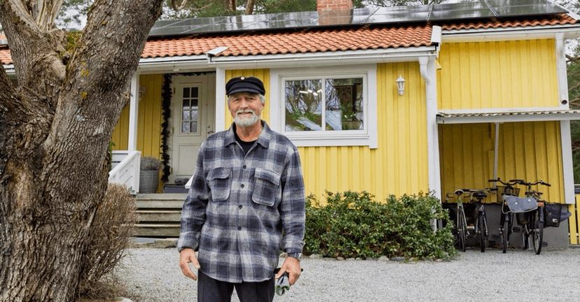 Pensionär som står framför sitt hus med solceller