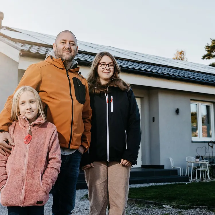 Paar mit Hund vor Einfamilienhaus mit Photovoltaikanlage auf dem Dach – nachhaltiger Solarstrom für das eigene Zuhause
