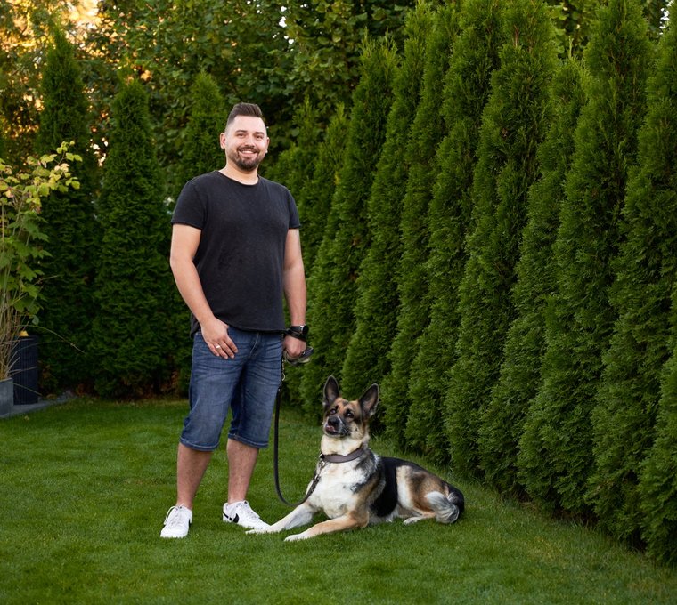 Hausbesitzer mit Hund im Garten vor Hecke – Beispiel für nachhaltiges Wohnen mit Solarenergie im eigenen Zuhause