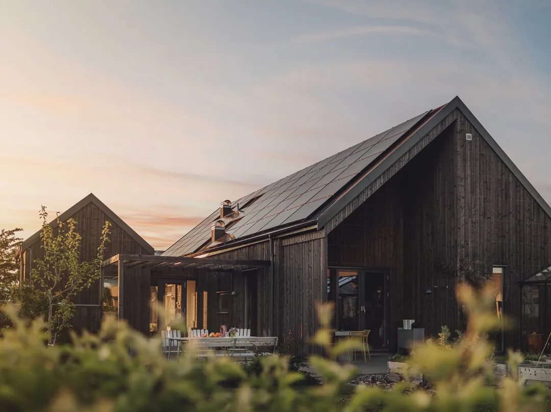 Modernes Holzhaus mit Solaranlage auf dem Dach in Abendsonne – nachhaltige Energie und Photovoltaiklösung von Svea Solar